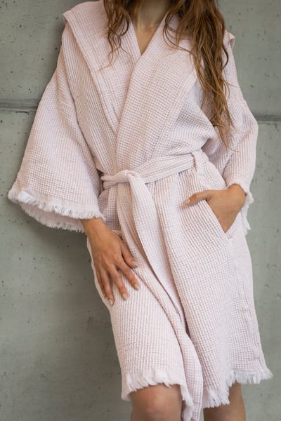 Abyss & Habidecor BEES 350gr: Vahvelkoes hele roosakasbeež hommikumantel naise seljas halli betoonseina taustal eestvaates