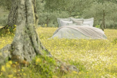 Celso de Lemos BIJOUX pillowcase: A bed with pale green and white pillows on a flowering meadow among olive trees