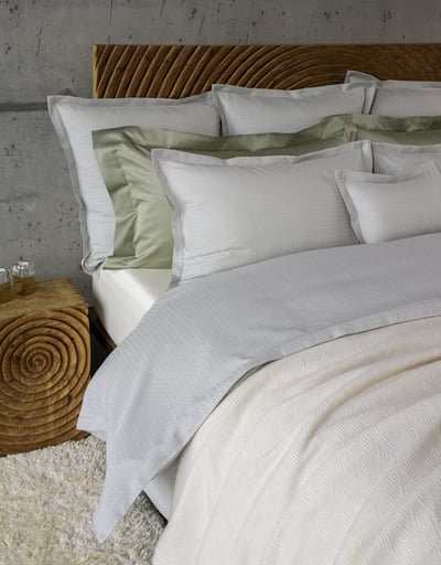 Celso de Lemos BIJOUX pillowcase: Grey flanged pillowcases and a green pillow in front of a carved wooden headboard