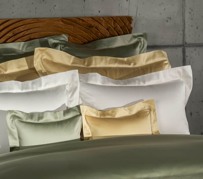 Celso de Lemos BOURDON duvet cover: A stack of green, gold and white pillowcases in front of a wooden headboard