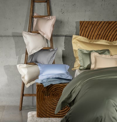 Celso de Lemos BOURDON duvet cover: Pink, grey and blue pillows on a wooden ladder, with a bed in an olive-green duvet cover beside