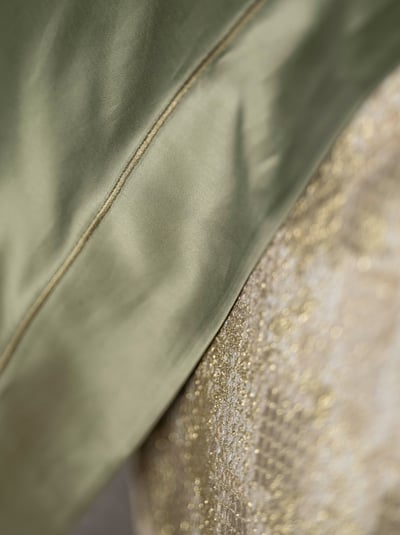 Celso de Lemos BOURDON duvet cover: Close-up of olive-green sateen and the embroidered line, with gold patterned fabric behind