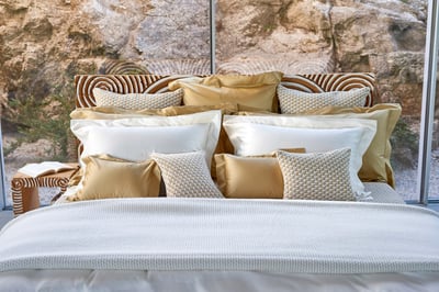 Celso de Lemos BOURDON duvet cover: A bed with gold and white pillows, a rock face beyond the window