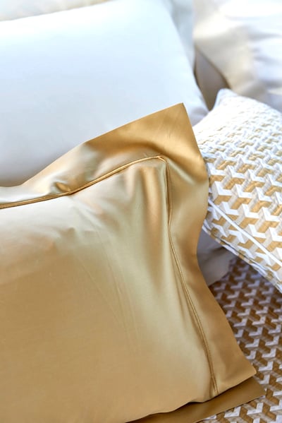 Celso de Lemos BOURDON duvet cover: Close-up of the corner of a gold pillowcase beside a white pillow and a patterned cushion