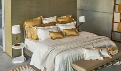Celso de Lemos BOURDON duvet cover: A bed with gold and cream pillows in a bedroom, with table lamps beside and a bench at the foot