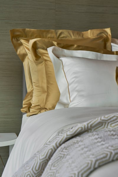 Celso de Lemos BOURDON duvet cover: Gold and white pillowcases in front of a grey headboard, with a grey patterned coverlet in front